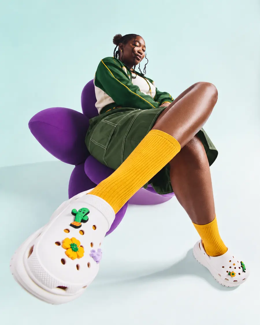 A young woman in a green varsity jacket and yellow socks lounging on a purple flower-shaped chair