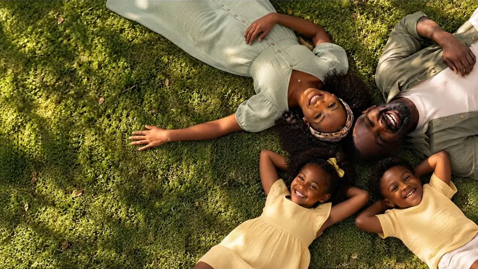A smiling family — mother, father, daughter and son — lying on the grass with their heads together