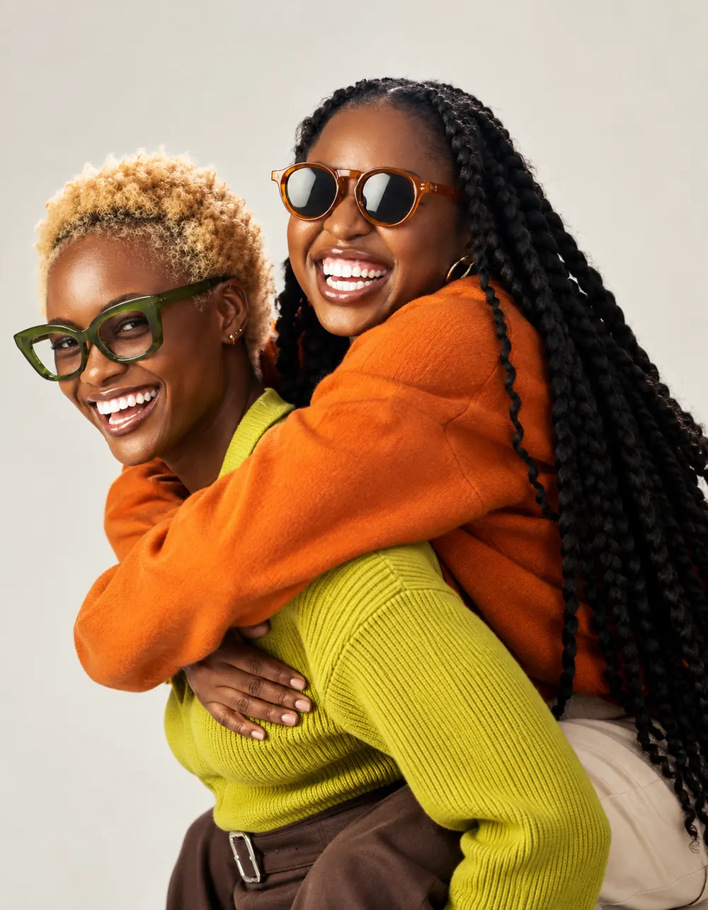 Two smiling friends in bright jumpers and glasses, one giving the other a piggyback